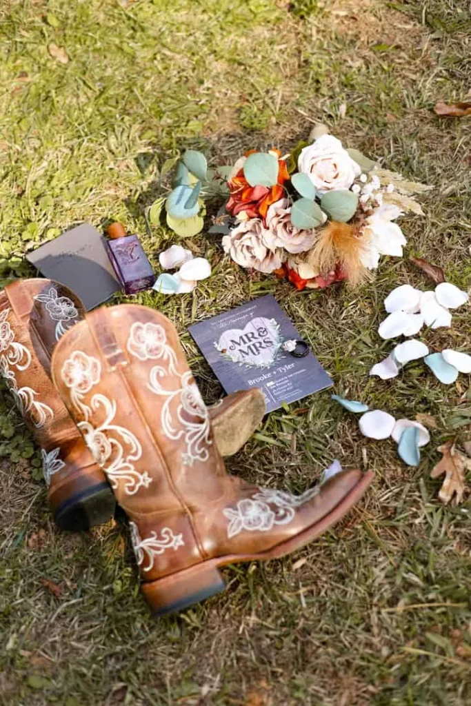Cowboy boots with floral embroidery and wedding accessories on grass.